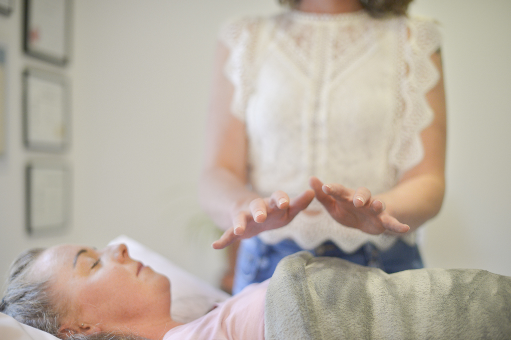 woman lying down with eyes closed as another woman stands over her providing reiki healing